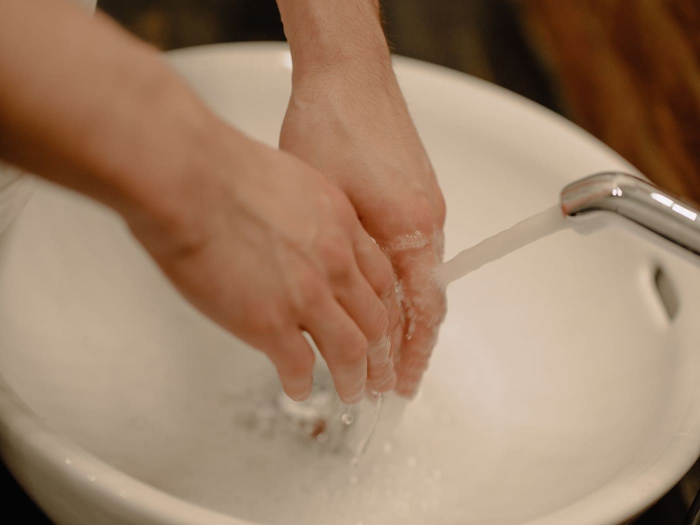 Hands being washed under running water in a white basin