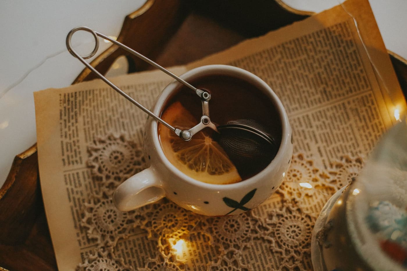 A cup of tea with a lemon slice and a tea infuser on a tray